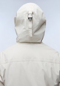 Giacca beige chiaro con collo alto e cappuccio regolabile, caratterizzata da un dettaglio in metallo a fibbia, texture liscia e cuciture visibili lungo le cuciture.