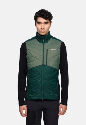 Groene gewatteerde vest met een hoge kraag, voorzien van chevron-quiltpatronen, ritszakken en een witte merklogo op de borst. Zwarte lange mouwen.