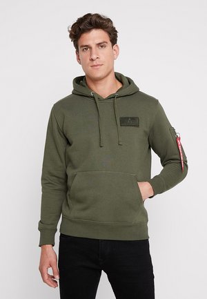 Sweat à capuche vert olive, avec une poche frontale, des poignets côtelés et une poche zippée sur le bras avec des détails rouges. Tissu au toucher doux.