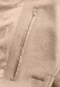 Beige wollen jas met een voorzak met rits en een gladde voering. De stof heeft een zachte textuur met een taillerende snit en minimale stiksels.