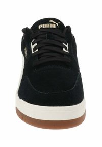 Zapatillas de ante negras con entresuela de goma blanca y suela marrón, con cordones negros y un logo dorado de Puma en la lengüeta.