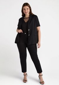 Svart kortärmad blazer med silverknappar, matchad med en svart transparente topp och tighta svarta byxor. Bärs med svarta remsandaler.