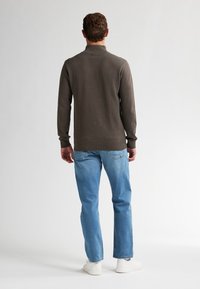 Maglione marrone a maglia con colletto alto, abbinato a jeans dritti azzurri chiari e sneakers bianche. Texture liscia, design aderente.