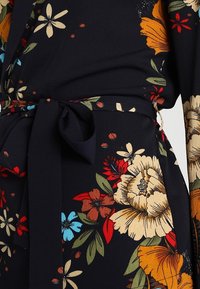 Abito a portafoglio floreale con sfondo blu navy scuro, grandi fiori colorati nelle tonalità di rosso, arancione, giallo e blu, con cintura abbinata da annodare.
