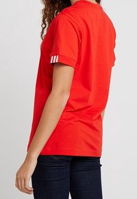 Röd bomullst-shirt med rund hals och korta ärmar. Har tre vita ränder på ärmen. Enkla, avslappnade design.