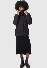 Black puffer jacket with a high collar, front zipper, and elastic drawstrings. Paired with a black ribbed skirt and black ankle boots.