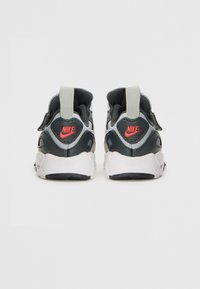 Nike cipők fekete és szürke dizájnnal, texturált felső résszel, fehér talppal, amelyen egy kiemelkedő piros logó található a sarkon, és egy textil húzófüllel.