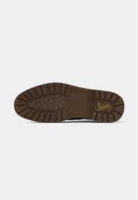 Suela de zapato de goma con un patrón de huella texturizado en marrón, con un logo central en amarillo y una zona de acolchado rectangular.