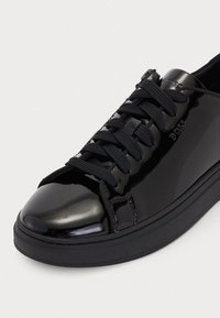 Kena musta madal sneaker mustade nööride ja 'BOSS' logoga küljel ja keelel, esitatud valgel taustal.
