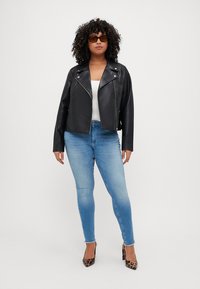 Black leather biker jacket with a cropped design, worn over a white top. Light blue skinny jeans and black leopard print heels complete the outfit.