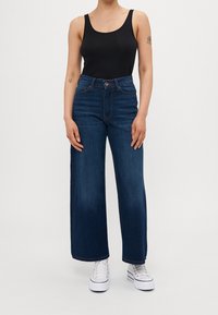 Korkea vyötärö, leveälahkeiset farkut tummansinistä denimkangasta. Varusteena nappikiinnitys, viisi taskua ja hienovaraisesti teksturoitu kangas. Yhdistetty mustan toppatakin kanssa.