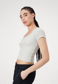 Siv t-shirt s kratkimi rokavi s rebrastim vzorcem in zaobljenim izrezom, v kombinaciji s temnimi hlačami z žepi. Gladka tekstura in oprijet dizajn.