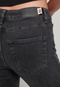 Jeans de mezclilla negra con un diseño ajustado, que cuentan con un parche de cuero en la cintura y un bolsillo trasero con un patrón de costura sutil.