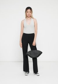Gray halter bodysuit, black flared pants, and a black handbag with a curved shape; model wears black sneakers. Plain white background.