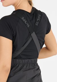 Schwarzer Sport-BH mit gekreuzten Trägern, versehen mit dem "SLOPE"-Logo; verbunden mit einem schwarzen elastischen Bund aus glatt gewebtem Material.