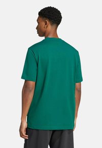 T-shirt di cotone verde, maniche corte, scollatura rotonda, vestibilità comoda, colore uniforme con una texture liscia. Nessun logo o design prominente visibile.