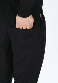 Czarne spodnie sportowe z zippowanym kieszeniem po boku. Materiał wydaje się gładki. Posiadają elastyczny pas oraz akcent w postaci szwedzkiej flagi.