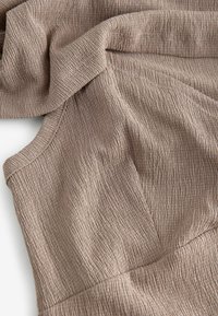 Tissu texturé et froissé de couleur marron clair, présentant de fines lignes verticales et un bord lisse. Drape doux et flexible.