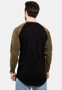 Crna i maslinasto zelena košulja dugih rukava, raglan stil, mekani materijal, s logom na leđima, zakrivljeni rub, nosi se s svijetloplavim trapericama.