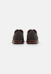 Dark brown suede shoes with a rounded toe, leather trim, and a stacked wooden heel. Minimalist design with no visible hardware or patterns.