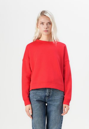 Rød kort sweatshirt med rund hals, senkede skuldre og lange ærmer. Kombinert med denimjeans. Ensfarget, glatt tekstur.