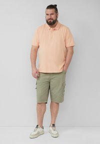 Licht perzikkleurig polo-shirt, olijfgroene cargoshorts met zakken, en neutrale sneakers. Casual pasvorm met korte mouwen en kraag.