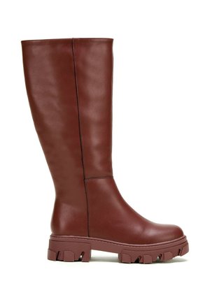 Wysoki brązowy skórzany but z grubą, protektorową podeszwą i prostym pionowym przeszyciem po bokach, widziany od zewnętrznej strony.