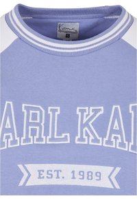 Jasnofioletowa bluza z białymi rękawami raglanowymi, z haftem w kolorze białym z napisem "KARL KANI" i "EST. 1989". Miękki materiał z mieszanki bawełny.