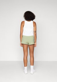 Top bianco a righe e pantaloni sportivi verde chiaro, di lunghezza corta, con texture liscia, indossati con calze bianche e sneakers, visti da dietro.