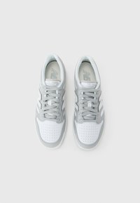 Sneaker bianchi e grigie realizzate in pelle e rete. Presentano una tomaia forata, lacci grigi e un marchio sulla linguetta. Design atletico classico.