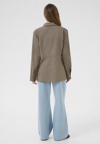 Brun, tekstureret blazer med en figursyet talje, lange ærmer og spids krave, parret med lyseblå, vide bukser.