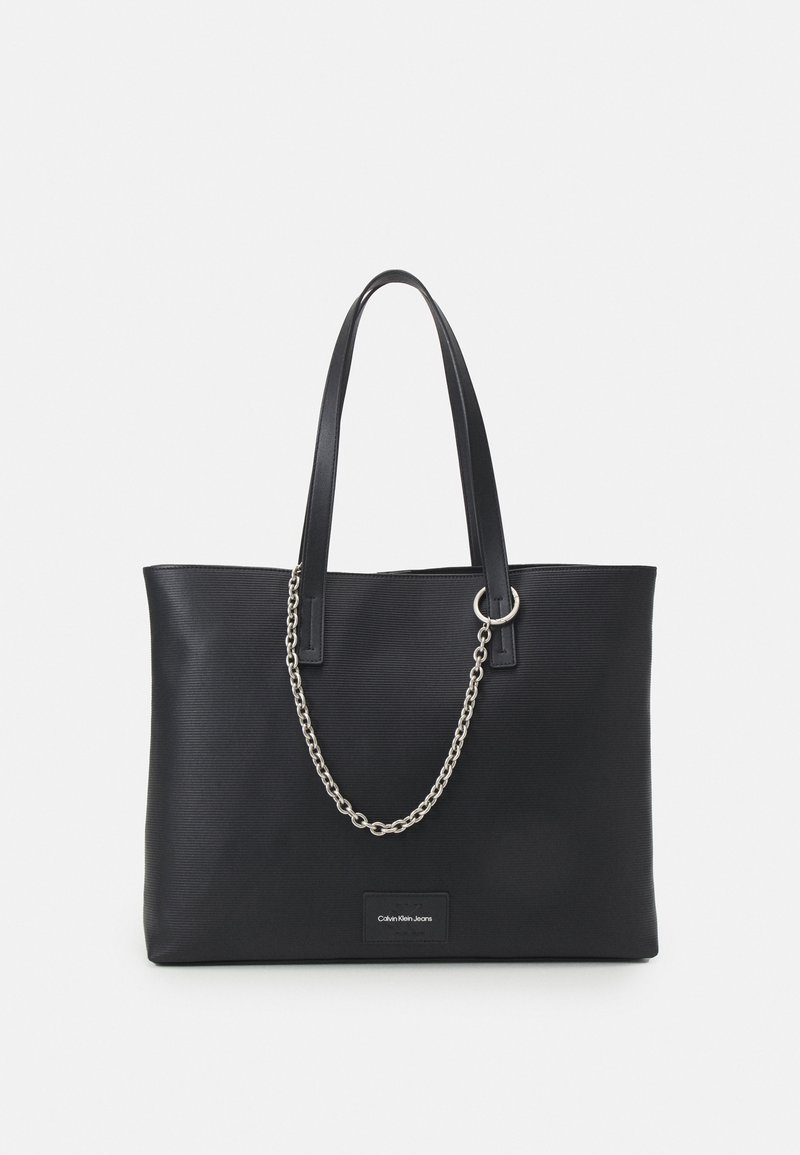 Sac cabas noir texturé avec deux longues anses, une courte chaîne argentée et une petite étiquette Calvin Klein Jeans au centre devant.