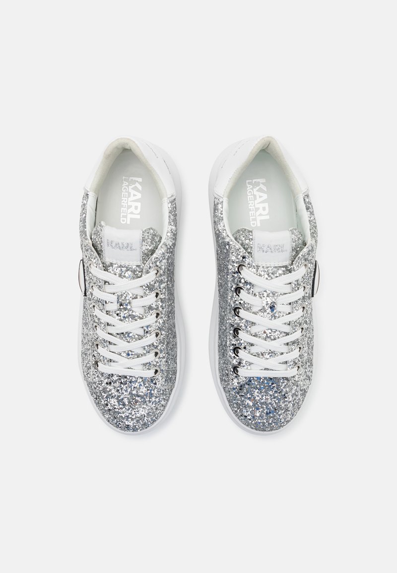 Zapatillas de lentejuelas plateadas con acentos blancos, cordones planos y un acabado texturizado. Presenta un detalle del logo en la lengüeta y el costado. Diseño de punta redondeada.