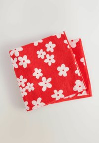 Röd handduk med vita blommönster, mjuk textur, rektangulär form, med en vikning som visar snygg söm.