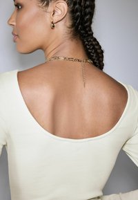 Long-sleeve off-white top with a wide neckline and ribbed texture; highlights a gold chain detail at the back, complementing the design.