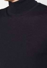 Maglione a collo alto di colore nero realizzato in un tessuto a maglia testurizzato. Presenta un piccolo logo impresso sul petto.