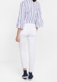 Vita, åtsittande byxor tillsammans med en ljusblå och vit randig blus med trumpetärmar, bärs med marinblå sneakers.