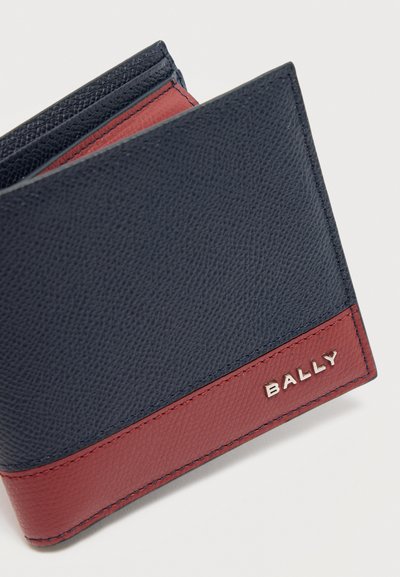Δερμάτινο δίπτυχο πορτοφόλι με μπλε επάνω μέρος και κόκκινο κάτω μέρος, με μεταλλικό λογότυπο Bally στο κόκκινο τμήμα.