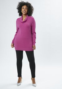 Maglione magenta a maglia con collo a pipistrello, polsini a coste e un pannello centrale con motivo, abbinato a leggings neri e tacchi alti argentati.