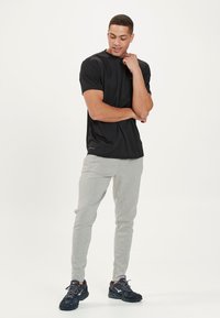 Schwarzes Kurzarmhemd aus leichtem Stoff, kombiniert mit hellgrauen Sporthosen und schwarzen Sportschuhen mit strukturiierter Außensohle.