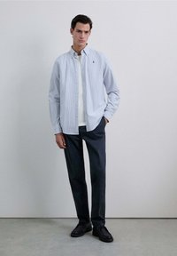 Lichtblauwe en witte gestreepte overhemd met knopen, gecombineerd met donkere broek en zwarte schoenen. Het overhemd heeft een standaard kraag en logo.
