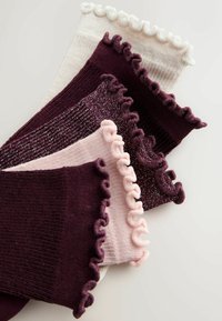 Fem par strømper med flæsekant i nuancer af hvid, pink og mørkelilla, med forskellig tekstur og et glitrende mønster.