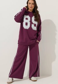 Burgundyröd huvtröja med stort silverfärgat nummer "89" på framsidan, kombinerad med matchande vida byxor med vita sidostråk. Blandning av bomull.