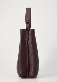 Sac à main en cuir bordeaux avec une surface texturée, une forme angulaire, une sangle réglable et une seule couture verticale sur le devant.