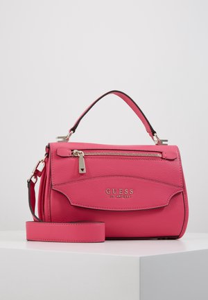 Sac à main Guess en cuir rose vif avec poignée supérieure, poche zippée à l'avant et bandoulière amovible, posé sur une surface blanche.