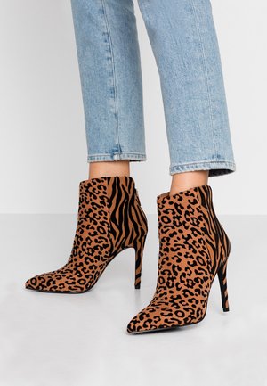 Personne portant un jean bleu clair et des bottines à talons hauts avec des motifs mélangés léopard et tigre.