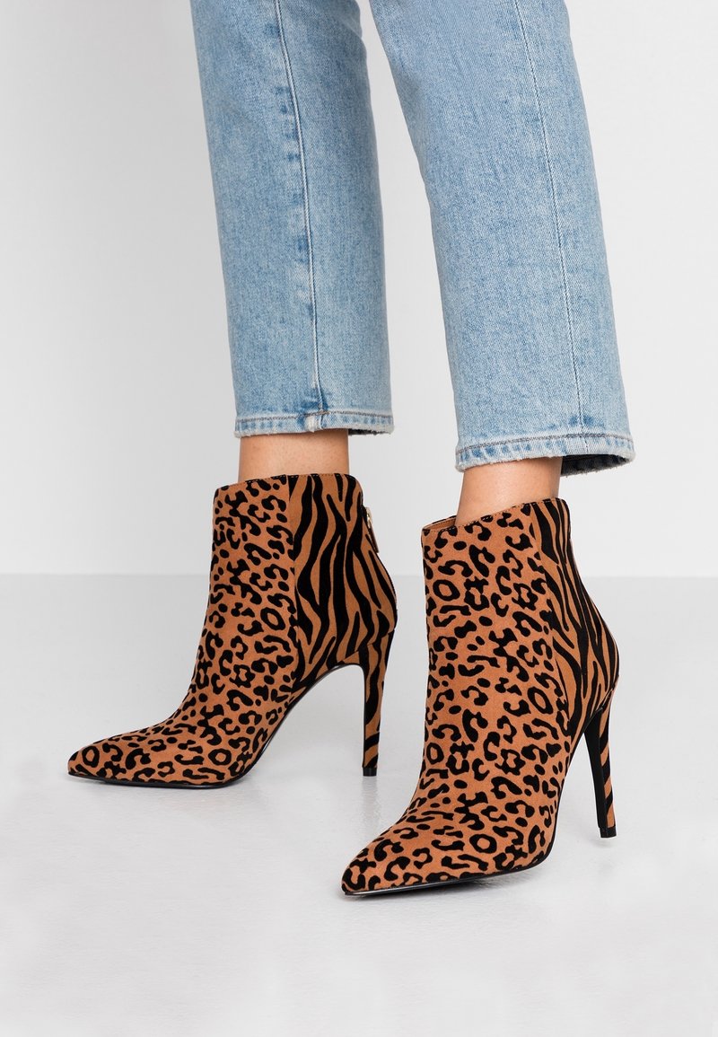 Personne portant un jean bleu clair et des bottines à talons hauts avec des motifs mélangés léopard et tigre.