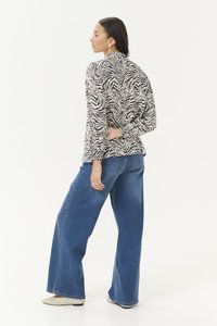 Long-sleeve shirt with a black and beige zebra print, paired with high-waisted, wide-leg denim jeans. Smooth fabric with gathered cuffs.