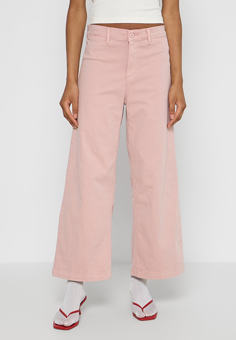Pantalons large en denim de coton rose, avec une fermeture à bouton sur le devant, des passants de ceinture et des détails de couture visibles.