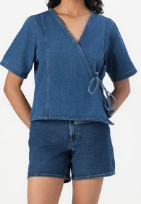 Denim wrap top with short sleeves, v-neck, and tie detail on the side. Paired with matching denim shorts. Both items are medium blue.